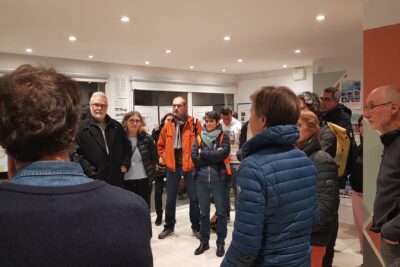 photo d'un pièce éclairée avec une trentaine de personnes visibles en photo, rassemblées en cercle - Agrandir l'image 2 sur 3, fenêtre modale