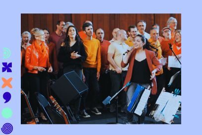 photo de groupe avec instruments de musique de la chorale de Samba Résille, aux vêtements aux couleurs chaudes orange, jaune, debout dans une salle tapissée de lambris - Agrandir l'image, fenêtre modale