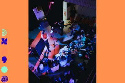 photo en plongée du parterre de public rassemblé autour d'une prestation musicale, de flûtiste debout au micro dans une salle plongée dans l'obscurité et les éclairages bleu et rose - Agrandir l'image, fenêtre modale