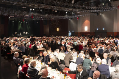 photo de la salle pleine de monde, à table, avec une décoration lumineuse au plafond et un groupe qui se produit sur scène à l'arrière plan - Agrandir l'image 7 sur 20, fenêtre modale