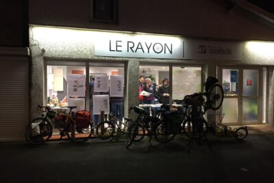 photo de la façade du local du Rayon, de nuit, on voit du monde à l'intérieur à travers les vitres, et plusieurs vélos, notamment cargo, dedans - Agrandir l'image 1 sur 3, fenêtre modale