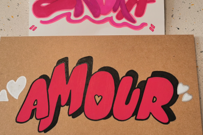zoom sur des lettrages en forme de graffiti réalisés au feutre sur du papier cartonné qsui indique en rose le mot "Amour" agrémenté de petits motifs en forme de coeur - Agrandir l'image, fenêtre modale