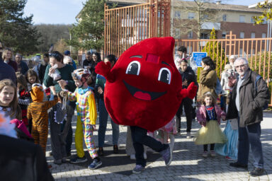 photo de familles sur la place en extérieur, au soleil, avec la mascotte du don du sang qui prend la pose pour l'objectif