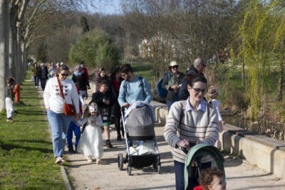 photo du défilé sur un chemin du parc de la Paderne, devant on voit un enfant déguisé en dragon sur une poussette à trois roues, derrière, d'autres familles et enfants déguisés - Agrandir l'image 3 sur 17, fenêtre modale