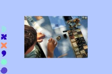 Photo en contre plongée d'un enfant assis à un plan de travail et maniuplant des caractères grévés sur des dominos de céramique, la scène baignée de tâches de lumière