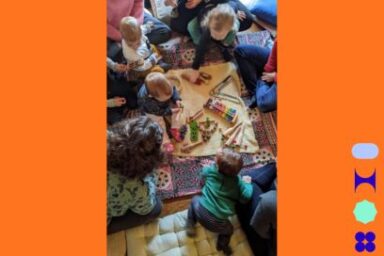 Photo prise en plongée de jeunes enfants installés sur des coussins autour d'un tapis de jeu dans une ambiance conviviale et détendue.