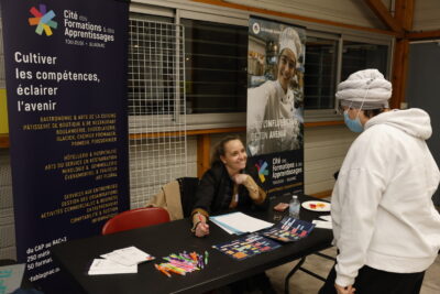 photo d'une personne qui échange avec une femme assise à un stand - Agrandir l'image 14 sur 22, fenêtre modale