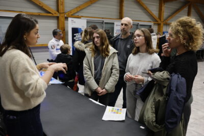 photo de deux jeunes femmes et deux adultes qui échangent avec une femme derrière un stand - Agrandir l'image 11 sur 22, fenêtre modale