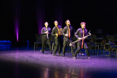 Le quatuor des Sourds-Doués s'avance en file indienne en effectuant des pas de danse comiques depuis la gauche de la scène