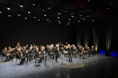 plan d'ensemble des musiciens de l'Orchestre d'Harmonie sur la scène de l'Escale, sous la lumière des projecteurs. - Agrandir l'image 5 sur 19, fenêtre modale