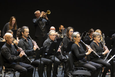 Le trompettiste debout à l'arrière-plan derrière le parterre de flûtistes assis, tous en tenues sombres et sobres. - Agrandir l'image 10 sur 19, fenêtre modale