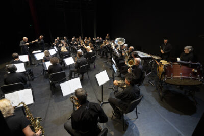 Les musiciens de l'Orchestre sur scène, de dos, assis derrière leur pupitre, attentifs au chef d'orchestre debout à gauche de l'image. - Agrandir l'image 6 sur 19, fenêtre modale