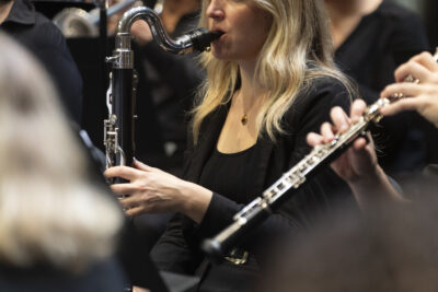 Plan rapproché sur une clarinettiste blonde aux cheveu lâchés, en tee-shirt noir à col rond, entourée d'autres clarinettistes. - Agrandir l'image 9 sur 19, fenêtre modale
