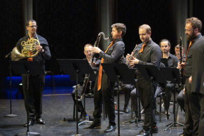 Debout, les musiciens des Sourds-Doués en costume noir et cravate orange satinée sur la scène, leurs instruments à la main. - Agrandir l'image 17 sur 19, fenêtre modale