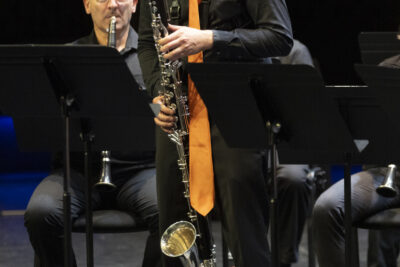 debout devant ses comparses musiciens assis tous en tenue sombre, le saxophoniste des Sourds-doués en train de souffler dans son instrument qui descend jusqu'à des pieds - Agrandir l'image 18 sur 19, fenêtre modale