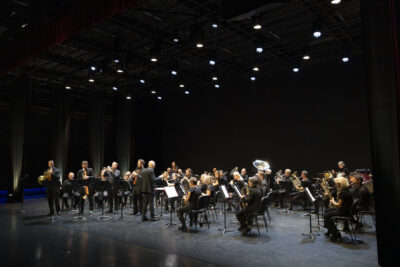 Photo d'ensemble en plein concert, de l'Orchestre dirigé par Claude Puysségur qui apparaît de dos accompagné du quatuor Les Sourds-Doués sur la scène de l'escale éclairée d'un myriade de projecteurs suspendus. - Agrandir l'image 19 sur 19, fenêtre modale