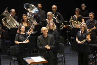Les musiciens de l'Orchestre d'Harmonie debout et souriants face au public, leurs instruments brillant dans la lumière - Agrandir l'image 4 sur 19, fenêtre modale