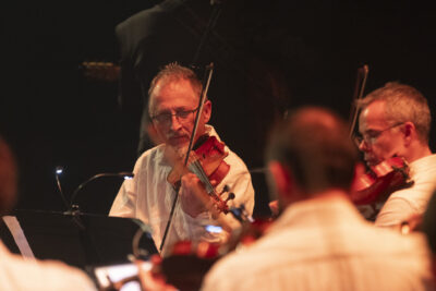 Gros plan sur les premier (Christian Loiseleur, de face) et deuxième (de profil, à droite de l'image) violons de l'orchestre l'air pénétré dans la lumière cuivrée au milieu du parterre des musiciens. - Agrandir l'image 10 sur 19, fenêtre modale