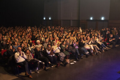 Vue sur le public nombreux en train d'applaudir et de sourire dans la faible lumière sépia - Agrandir l'image 18 sur 19, fenêtre modale