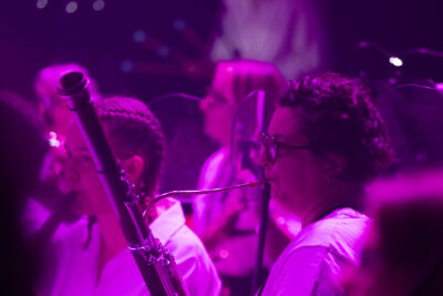 Plan rapproché dans une intense lumière pourpre sur deux joueuses de hautbois de profil dont la plus jeune à gauche porte des cheveux tressés sur le haut du crâne, avec effet floûté. - Agrandir l'image 19 sur 19, fenêtre modale