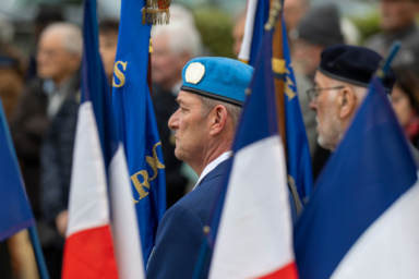 photo paysage de porte drapeaux à une cérémonie de commémoration, vus de derrière en biais avec les drapeaux français au premier plan