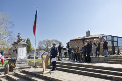 photo d'un officiel en uniforme debout devant le pupitre et micro, avec derrière lui l'orchestre d'une dizaine de musiciens en train de jouer - Agrandir l'image 11 sur 16, fenêtre modale