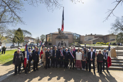 photo d'une trentaine de personnes rassemblées dehors, devant le monument aux morts, au centre des élus avec l'écharpe, le ciel est bleu - Agrandir l'image 16 sur 16, fenêtre modale