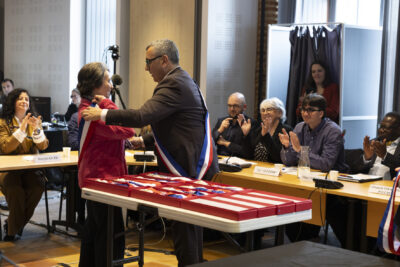 photo du Maire debout qui porte l'écharpe et la met à une élue debout devant lui - Agrandir l'image 7 sur 16, fenêtre modale