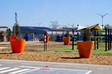 photo du square éphémère sous un beau ciel bleu, on voit les aménagements paysagers au sol (surface désimperméabilisée) et des grands pots avec des plantes dedans, et sur la droite un espace sportif avec notamment des barres de traction