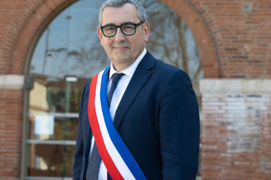 Photo portrait du Maire portant l'écharpe devant l'Hôtel de ville