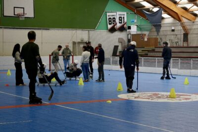 photo dans un gymnase, une quinzaine de personnes en roller et chaussures normales participent à un atelier, deux personnes sont sur des sortes de chariots à roues - Agrandir l'image 6 sur 16, fenêtre modale