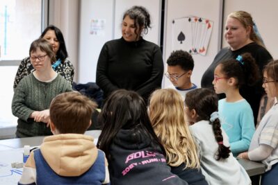 Photo d'un atelier dans une école, des enfants réunis autour d'une table avec des femmes adultes et une jeune femme autiste - Agrandir l'image 14 sur 16, fenêtre modale