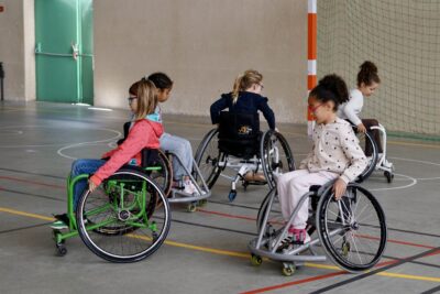 photo de cinq jeunes filles en fauteuil dans un gymnase, en train d'avancer en faisant tourner les roues - Agrandir l'image 11 sur 16, fenêtre modale