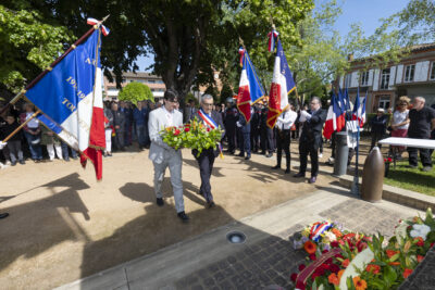photo du Maire Frédéric Parre et d'un homme qui portent une gerbe de fleurs pour les déposer avec les autres au sol, dans le square ensoleillé, avec les porteurs de drapeaux de chaque côté - Agrandir l'image 20 sur 26, fenêtre modale