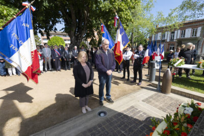 photo d'un homme et d'une femme debout qui se recueillent devant les gerbes de fleurs au sol et entre deux rangées de porteurs de drapeaux - Agrandir l'image 25 sur 26, fenêtre modale