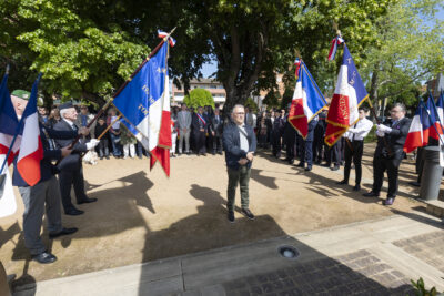 photo d'un homme qui se recueille dans le square avec les porteurs de drapeau de chaque côté et les élus derrière - Agrandir l'image 24 sur 26, fenêtre modale