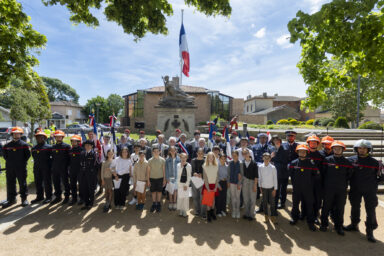 photo de groupe des élus, enfants, institutionnels rassemblés devant le monument aux morts, au soleil