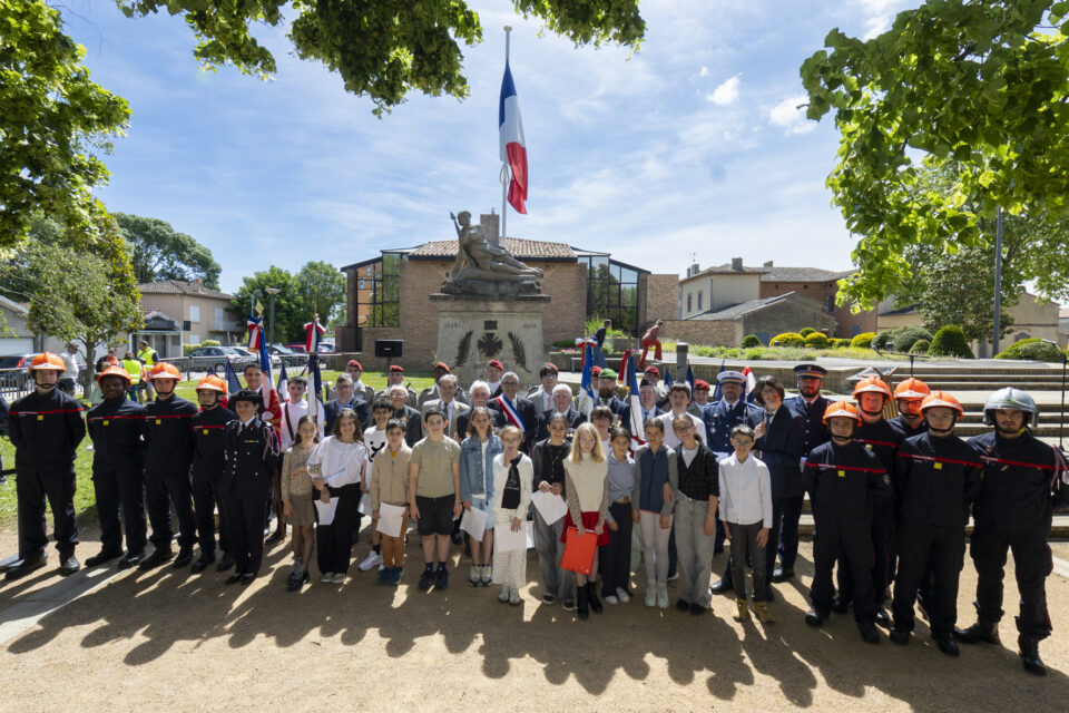 photo de groupe des élus, enfants, institutionnels rassemblés devant le monument aux morts, au soleil