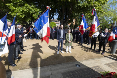 photo d'un homme et d'une femme qui se recueillent dans un square ensoleillé, de chaque côté il y a les porteurs de drapeaux - Agrandir l'image 22 sur 26, fenêtre modale