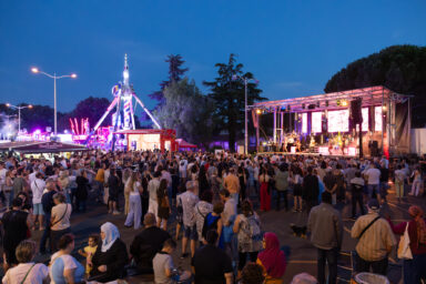 photo le soir de la fête locale, avec vue sur la foule, et à l'arrière-plan à gauche un manège, à droite la scène de cp,cert