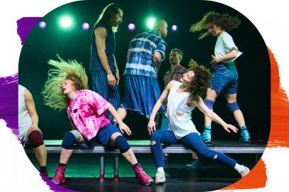 Cette image capte un moment particulièrement énergique et presque explosif de la chorégraphie. Au premier plan, deux danseuses dominent la scène par des mouvements très amples. À gauche, l’une projette sa tête en arrière, ses cheveux volant dans un arc spectaculaire, ce qui donne une forte sensation de vitesse et de relâchement. À droite, une autre est dans une posture étirée et déséquilibrée, une jambe tendue, le torse incliné, les bras relâchés, comme prise dans un mouvement de chute contrôlée. Derrière elles, plusieurs danseurs sont debout sur la plateforme. Leurs attitudes sont plus contenues mais restent expressives : l’un se tient droit et regarde vers le bas, un autre tourne le dos partiellement, tandis qu’un troisième semble pris dans une interaction ou une transition de mouvement. - Agrandir l'image, fenêtre modale