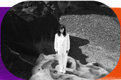 vue d'ensemble PHOTO ARTY EN NOIR ET BLANC jouant sur ombres et lumière, de l'artiste debout vêtue d'un costume blanc au milieu d'un paysage très minéral, cheveux bruns ondulés lâchés sur les épaules chaussées de lunettes noires. - Agrandir l'image, fenêtre modale