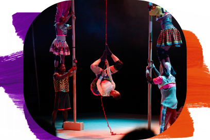 On voit une scène de spectacle prise en plongée (vue d’en haut), avec plusieurs artistes disposés autour d’une performance centrale. Deux longs poteaux horizontaux sont maintenus en hauteur par des artistes de chaque côté. Au-dessus de ces barres, une performeuse est en équilibre : son corps est allongé en travers, légèrement cambré, avec une jambe accrochée et l’autre étendue, tandis qu’un bras pend vers le bas. Sa posture donne une impression de fluidité et de contrôle. Autour d’elle, d’autres artistes participent activement : certains tiennent les barres, d’autres sont à genoux ou debout en dessous, comme pour soutenir ou accompagner la figure centrale. Au sol, des confettis rouges sont dispersés, ajoutant une touche festive et visuelle à la scène. - Agrandir l'image, fenêtre modale