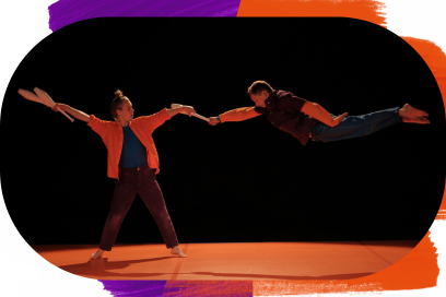 Deux acrobates sur scène inondée de lumière orange, les deux portent une étoffe orange, coordonnée à un tee-shirt et un pantalon bleu ou violet, comme deux jumeaux habillés pareils sans l'être tout à fait; à gauche le jongleur aux cheveux blancs ramassés en queue de cheval tient des quilles blanches de la main droite et son acolyte de la main gauche, qui ce dernier effectue un saut et se trouve en position horizontale gainé sur une ligne parallèle au sol dans un mouvement saisi par le photographe. - Agrandir l'image, fenêtre modale
