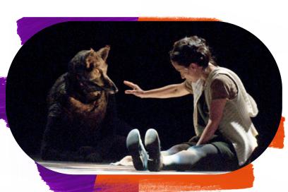 Sur une scène sombre, une personne drapée de blanc et portant un masque de loup est assise face à une femme assise au sol qui la regarde intensément. - Agrandir l'image, fenêtre modale
