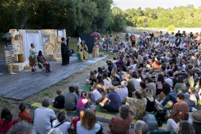 photo d'un spectacle dans un parc, sur la scène quatre personnes en costumes, font face à fr nombreux spectateurs assis dans l'herbe - Agrandir l'image 3 sur 15, fenêtre modale