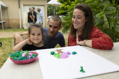 une petite fille et un homme et une femme adultes sourient à l'objectif alors qu'ils jouent à un jeu sur une table - Agrandir l'image 5 sur 14, fenêtre modale