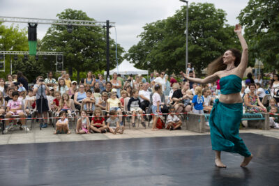 photo du spectacle de danse tahitienne avec derrière la danseuse seule sur scène en tenue verte, les familles rassemblées, assises pour voir le spectacle - Agrandir l'image 10 sur 14, fenêtre modale