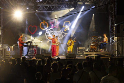 photo d'un concert, de nuit, un groupe de 5 jeunes sur scène en vêtements colorés - Agrandir l'image 13 sur 14, fenêtre modale