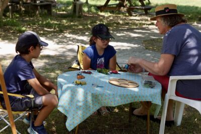 photo de deux enfants à table avec une personne adulte, dans un parc à l'ombre - Agrandir l'image 14 sur 19, fenêtre modale